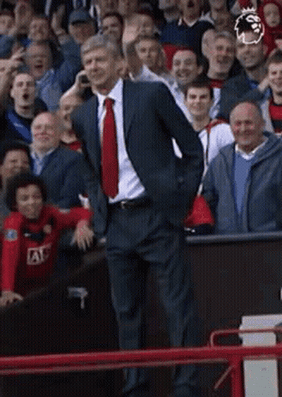 A Man In A Suit And Tie Is Talking On A Cell Phone While Standing In Front Of A Crowd Of People . GIF