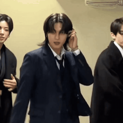 A Man In A Suit And Tie Is Talking On A Cell Phone While Standing Next To Two Other Men In Suits . GIF