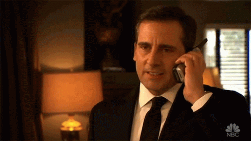 A Man In A Suit And Tie Is Talking On A Cell Phone With The Nbc Logo Visible GIF