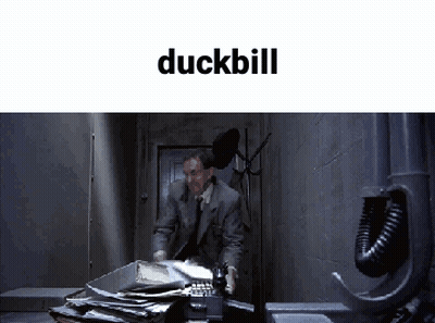 A Man In A Suit And Tie Is Talking On A Phone In A Dark Room With The Word Duckbill Above Him GIF