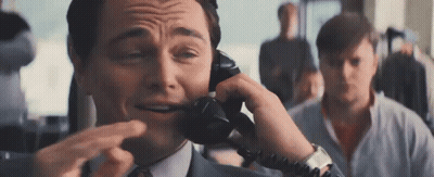 A Man In A Suit And Tie Is Talking On A Telephone While Making A Funny Face . GIF