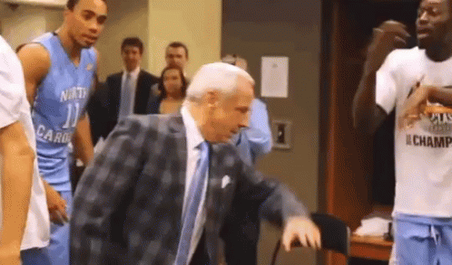 A Man In A Suit And Tie Is Talking To A Basketball Player In A North Carolina Uniform .. GIF