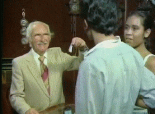 A Man In A Suit And Tie Is Talking To A Man And A Woman . GIF