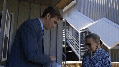 A Man In A Suit And Tie Is Talking To A Woman In A Blue And White Dress GIF