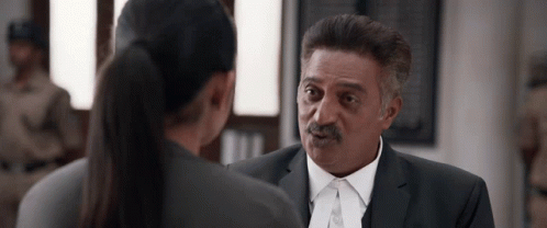 A Man In A Suit And Tie Is Talking To A Woman In A Ponytail GIF