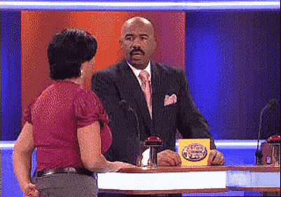 A Man In A Suit And Tie Is Talking To A Woman In A Red Shirt On A Game Show GIF