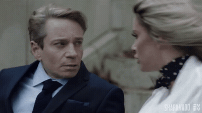 A Man In A Suit And Tie Is Talking To A Woman In A White Shirt . GIF