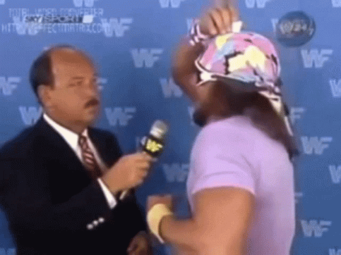 A Man In A Suit And Tie Is Talking To A Wrestler In A Purple Shirt While Holding A Microphone . GIF