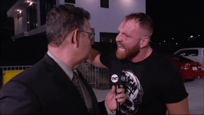 A Man In A Suit And Tie Is Talking To Another Man In A Black Shirt That Says Tnt GIF