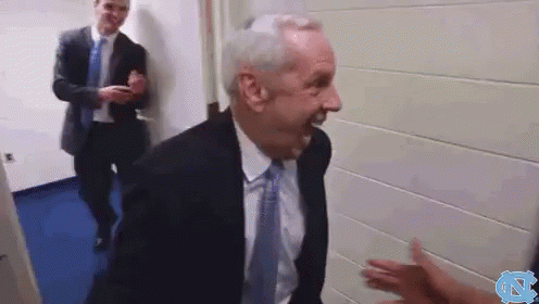 A Man In A Suit And Tie Is Talking To Another Man In A Hallway GIF