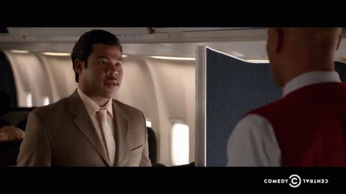 A Man In A Suit And Tie Is Talking To Another Man In A Red Vest Which Says Comedy Central GIF