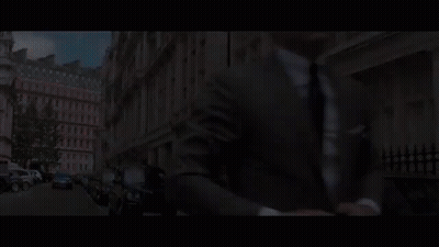 A Man In A Suit And Tie Is Talking To Another Man In A Room With A Sign In A Foreign Language GIF