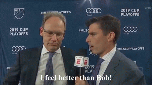 A Man In A Suit And Tie Is Talking To Another Man In Front Of A Banner That Says Mls Cup Playoffs GIF