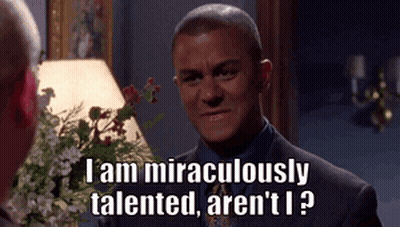 A Man In A Suit And Tie Is Talking To Another Man In Front Of A Lamp And Flowers . GIF