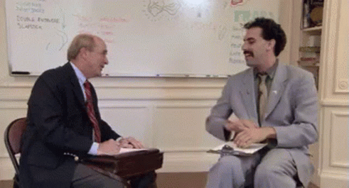 A Man In A Suit And Tie Is Talking To Another Man In Front Of A White Board GIF