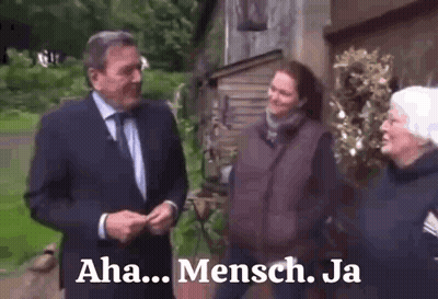 A Man In A Suit And Tie Is Talking To Two Women In Front Of A Building With The Words Aha Mensch Ja On The Bottom GIF