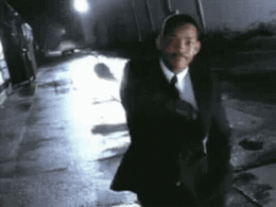 A Man In A Suit And Tie Is Walking Down A Dark Street At Night . GIF