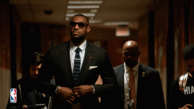 A Man In A Suit And Tie Is Walking Down A Hallway GIF
