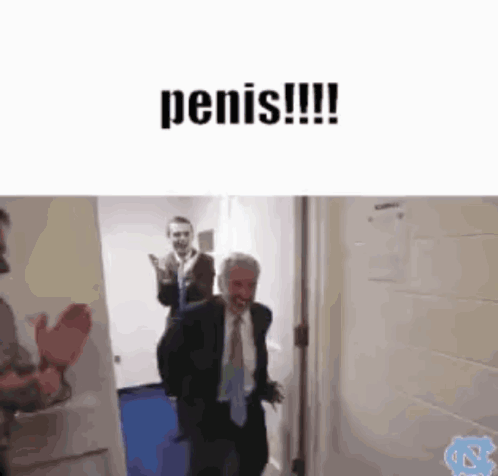 A Man In A Suit And Tie Is Walking Down A Hallway While Another Man Applauds Behind Him . GIF