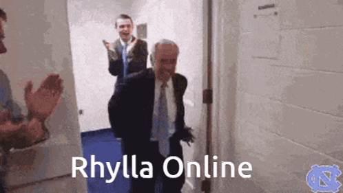 A Man In A Suit And Tie Is Walking Down A Hallway With The Words Rhylla Online Written On The Bottom GIF