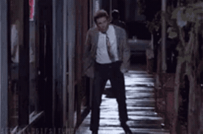 A Man In A Suit And Tie Is Walking Down A Narrow Alleyway At Night . GIF