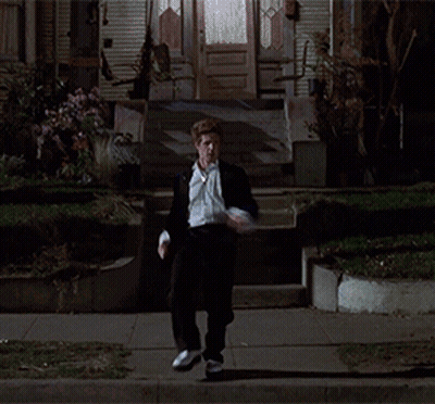 A Man In A Suit And Tie Is Walking Down A Street At Night GIF