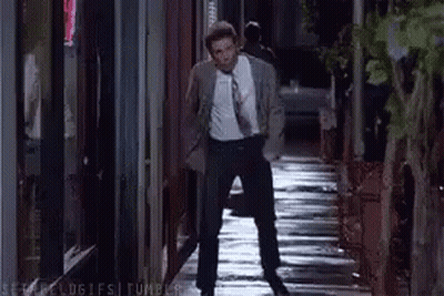 A Man In A Suit And Tie Is Walking Down A Wet Sidewalk At Night . GIF