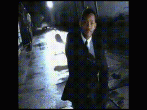 A Man In A Suit And Tie Is Walking Down A Wet Street GIF