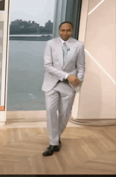 A Man In A Suit And Tie Is Walking Down A Wooden Floor . GIF