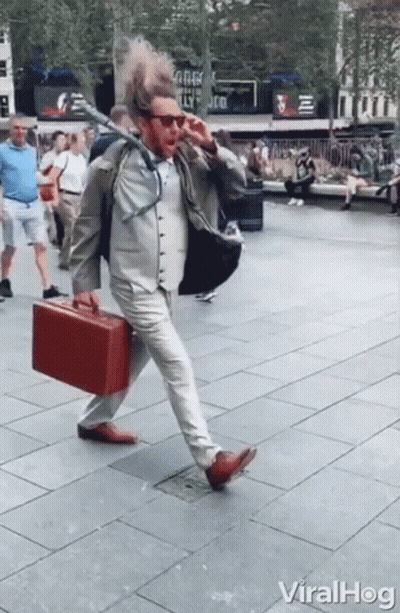 A Man In A Suit And Tie Is Walking Down The Street With A Red Briefcase In His Hand GIF