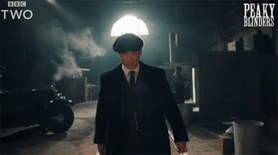 A Man In A Suit And Tie Is Walking In A Dark Room With Peaky Blinders Written On The Bottom Of The Screen GIF