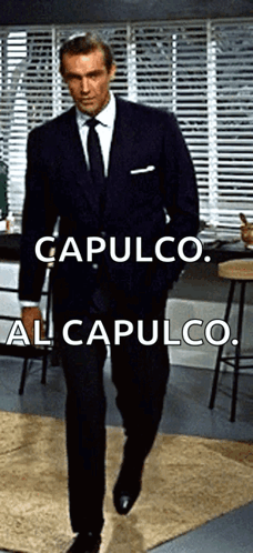A Man In A Suit And Tie Is Walking In A Room With The Words Capulco Al Capulco Below Him GIF