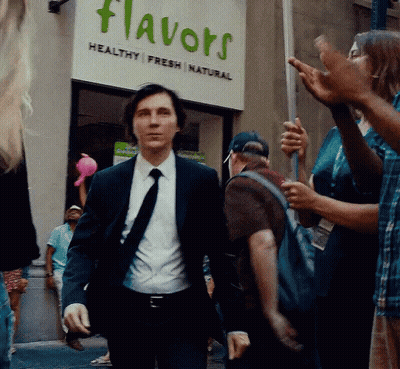 A Man In A Suit And Tie Is Walking In Front Of A Flavors Sign GIF