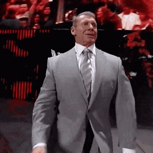 A Man In A Suit And Tie Is Walking On A Stage . GIF
