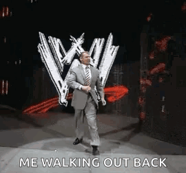 A Man In A Suit And Tie Is Walking On A Stage In Front Of A Sign That Says `` Me Walking Out Back '' . GIF