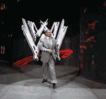 A Man In A Suit And Tie Is Walking On A Stage In Front Of A W Logo GIF