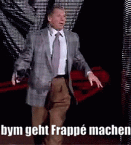 A Man In A Suit And Tie Is Walking On A Stage With The Words Bym Geht Frappe Machen On The Bottom . GIF