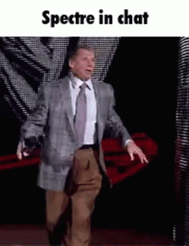 A Man In A Suit And Tie Is Walking On A Stage With The Words Spectre In Chat Below Him . GIF
