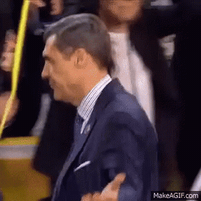 A Man In A Suit And Tie Is Walking Through A Crowd . GIF