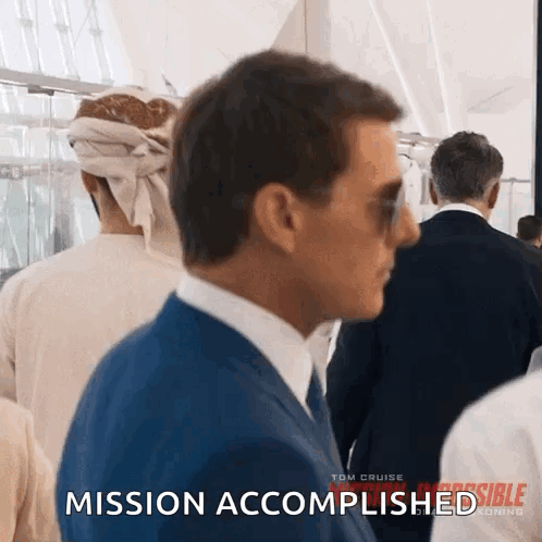 A Man In A Suit And Tie Is Walking Through A Crowd Of People And Says Mission Accomplished . GIF