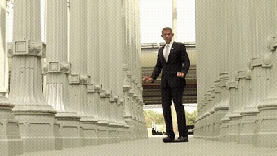 A Man In A Suit And Tie Is Walking Through Columns GIF