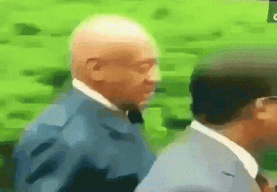 A Man In A Suit And Tie Is Walking With Another Man GIF