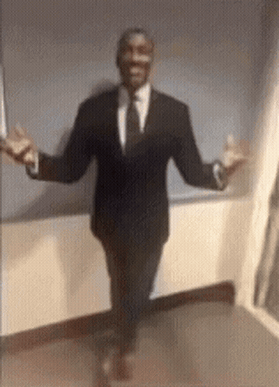 A Man In A Suit And Tie Is Walking With His Arms Outstretched . GIF