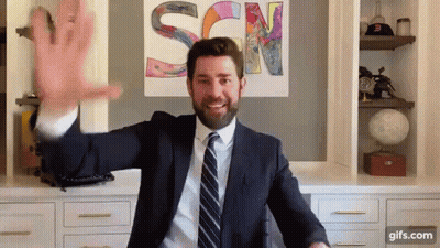A Man In A Suit And Tie Is Waving His Hand In Front Of A Sign That Says Scn GIF