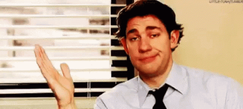 A Man In A Suit And Tie Is Waving His Hand In Front Of A Window With Blinds . GIF