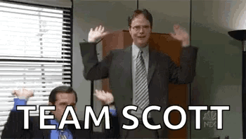 A Man In A Suit And Tie Is Waving His Hands In The Air In Front Of A Window . GIF