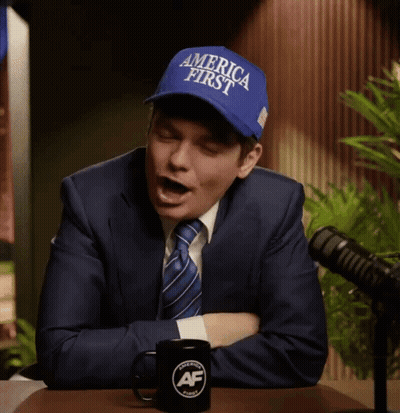 A Man In A Suit And Tie Is Wearing A Blue Hat That Says America First GIF