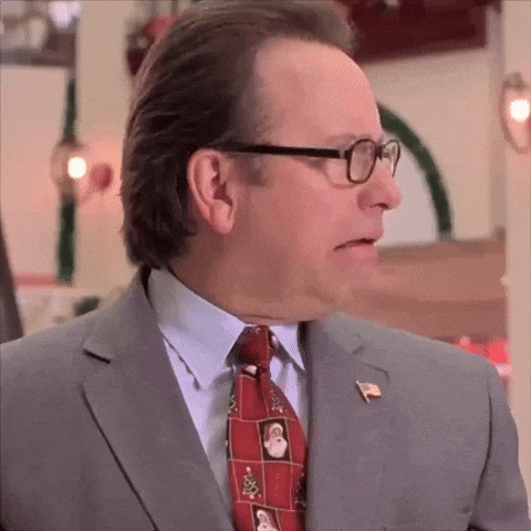 A Man In A Suit And Tie Is Wearing Glasses And A Pin GIF