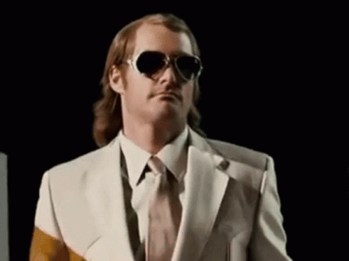 A Man In A Suit And Tie Is Wearing Sunglasses And Making A Funny Face . GIF