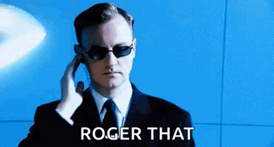 A Man In A Suit And Tie Is Wearing Sunglasses And Talking On A Phone . GIF